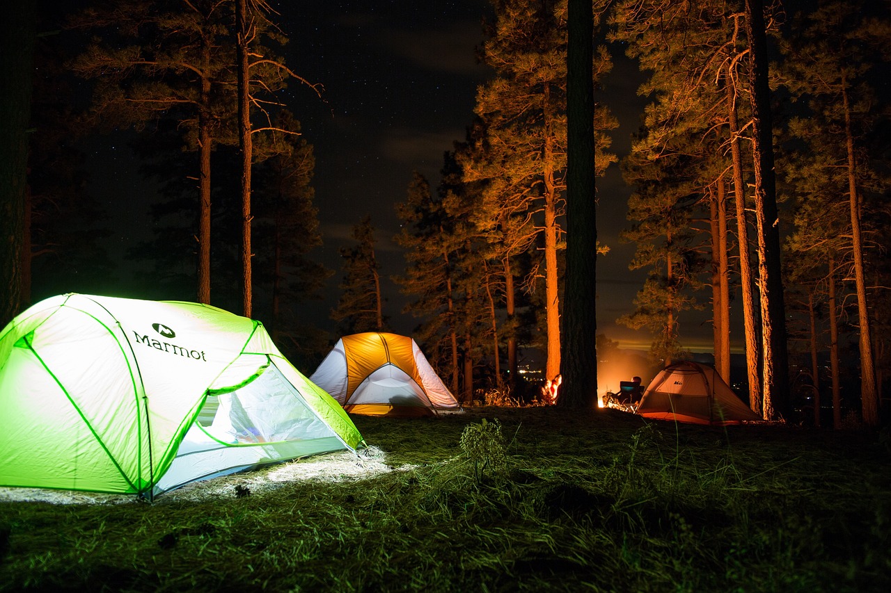 3 tents set up around a campsite at nighttime with light glow from the bonfire