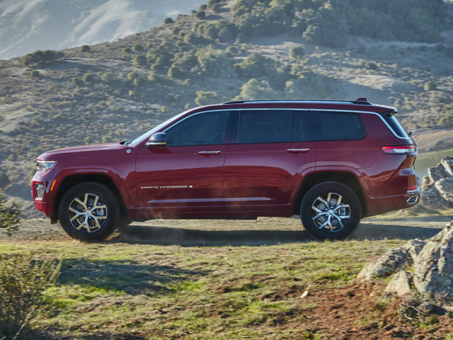 Drivers side view of a red 2024 Jeep Grand Cherokee L parked aside a mountain at dusk