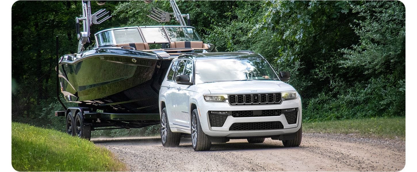 White 2026 Jeep Grand Cherokee Summit towing a boat down a dirt road, a Grand Cherokee for Bowie, TX lake weekends